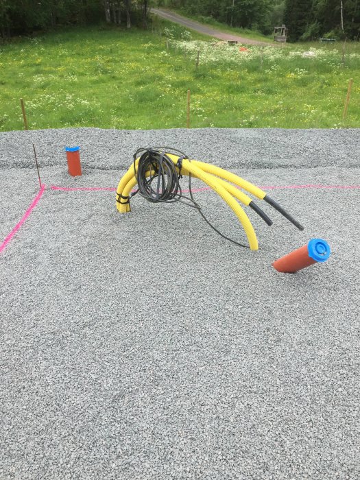 Grusad yta med markeringspinnar och böjda gula slangar samt el-kabel rullade på marken.