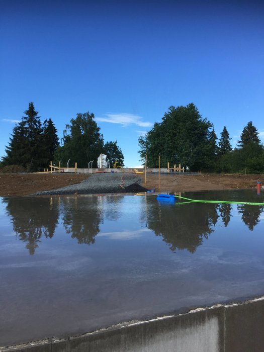 Grundgjutning i byggprojekt, nyligen gjutet betonggolv med vattenspegling och blå himmel.