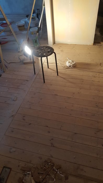 Renovering av ett rums trägolv med verktyg och byggavfall på golvet och en arbetslampa tänd.