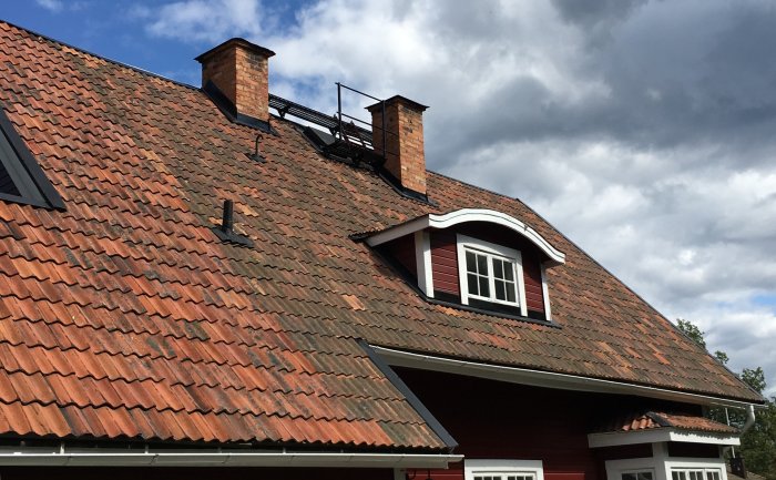 Tak med tegelpannor på en byggnad, inklusive takfönster och en skorsten under molnig himmel.