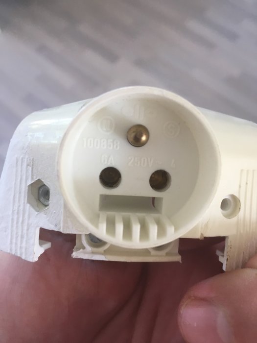 Elektrisk kontakt med tre stift, varav ett för jordning, hållen i hand.