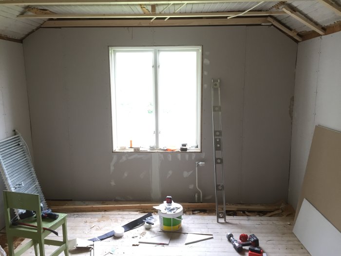 Ett rum under renovering med gipsskivor på två tredjedelar av väggarna, verktyg och byggmaterial på golvet.