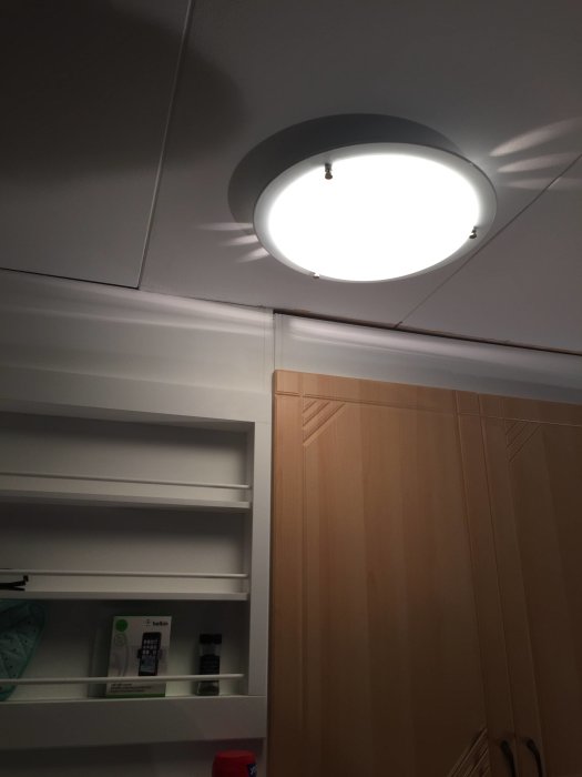 Modern rund plafond i taket bredvid vita köksskåp och ett träfärgat köksskåp, belyst och påslagen.