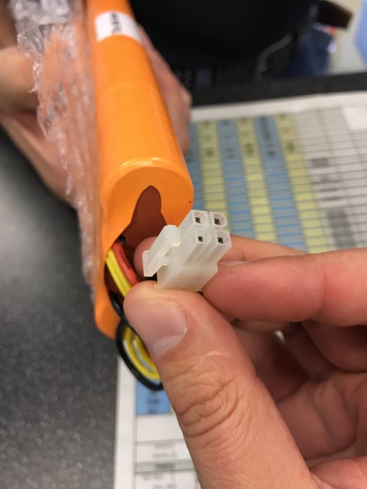 Hand håller en plastkontakt framför en orange batteripack för att visa önskad koppling till robotgräsklippare.