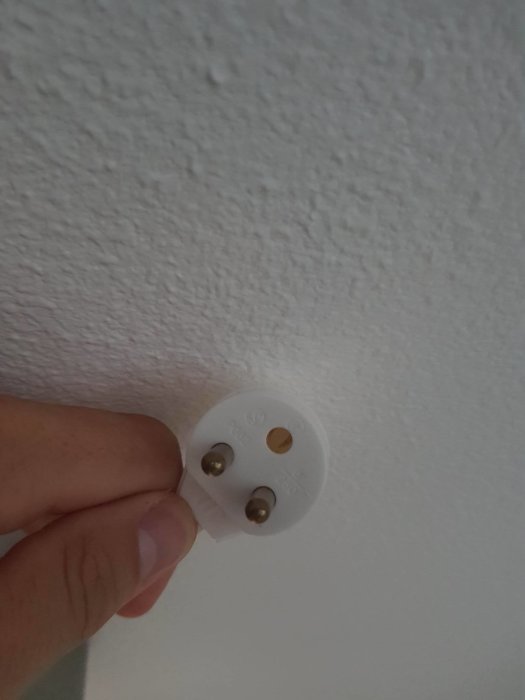 Hand försöker ta bort en vit strömkontaktskåpa utan synlig skruv från en vägg.