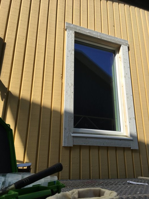 Nytt fönster installerat i gult trähus, verktyg syns i förgrunden.