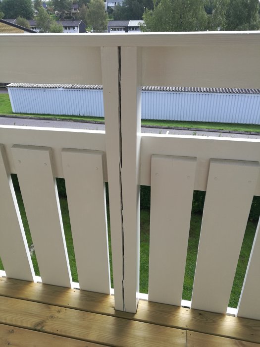En vertikal spricka i en vitmålad stolpe på en balkong med utsikt över en trädgård.