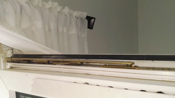 Närbild på övre delen av balkongdörrens låsanordning med skena och låsmekanism.