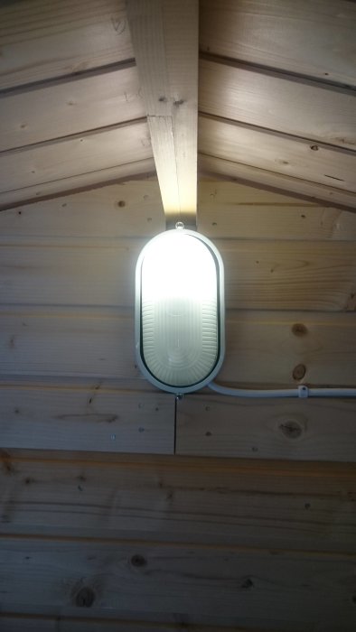 LED-armatur monterad på trävägg, synlig sockel och elektronik under upplyst del.