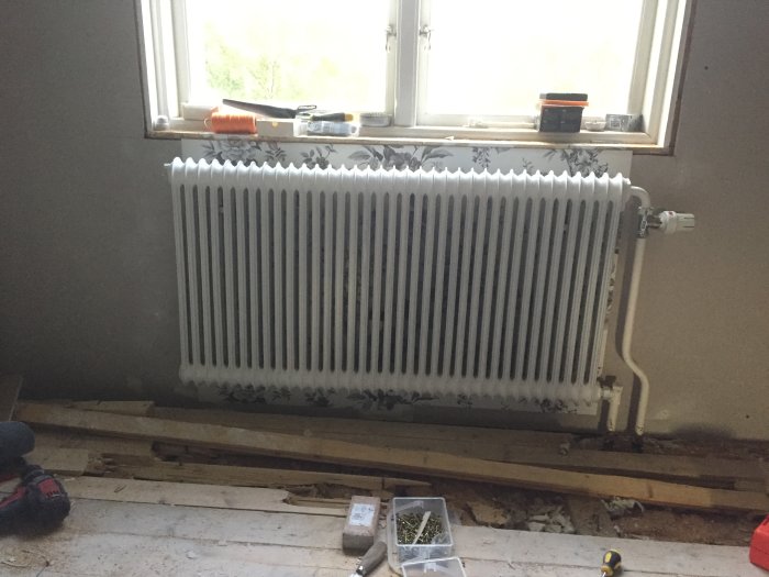 Ny tapetserad vägg med monterad vit radiator framför ett fönster och verktyg på golvet.
