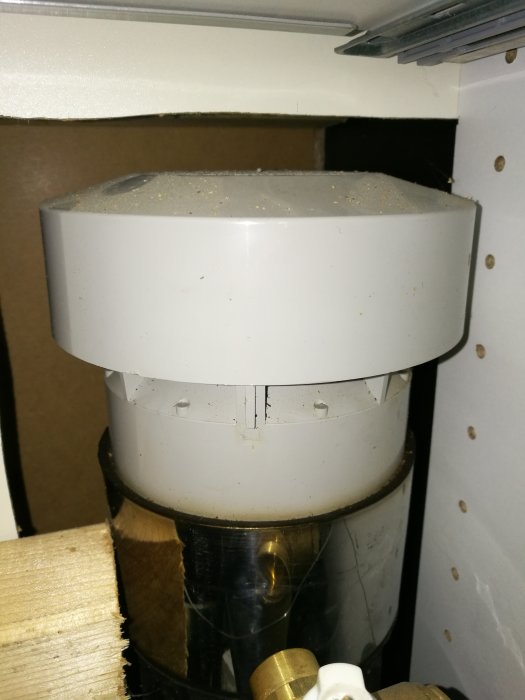 Rund vit plastkåpa som möjligen täcker ett gammalt avloppsrör, placerat bakom köksskåp.
