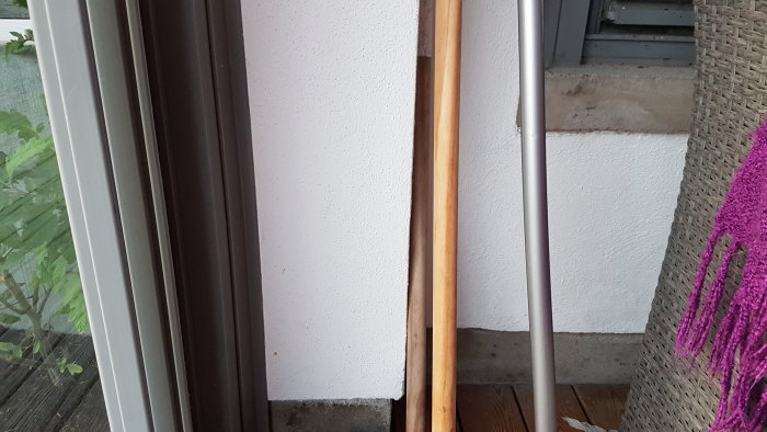 Hörnan av ett inglasat uterum med synlig trätrall och en vit putsad betongvägg intill dörrkarmen.