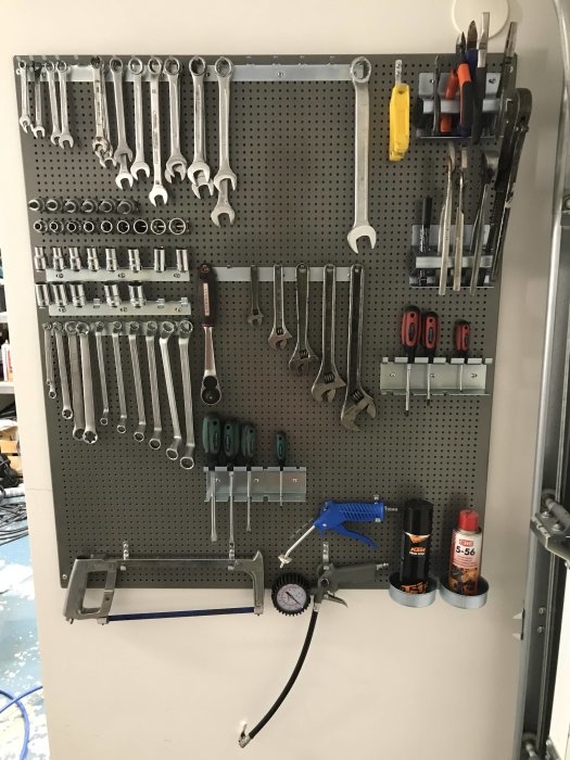 Verktygstavla med upphängda skiftnycklar, skruvmejslar, tänger och andra verktyg i ett garage.