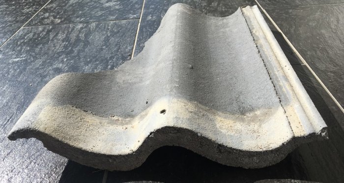 En tvåkupig grå betongtakpanna mot en mörk bakgrund, som matchar mått för Benders, Monier, S:t Eriks.