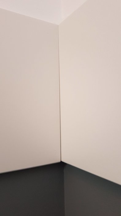 Spricka i hörnet där två vita väggar och mörkt golv möts i ett nymålat hus.