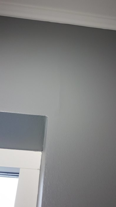 Spricka i gråmålad vägg ovanför en dörrkarm, synliga fel trots målning.