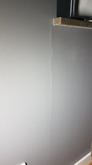 Spricka på en nymålad vägg som går från takkanten nedåt, bredvid en hörna.