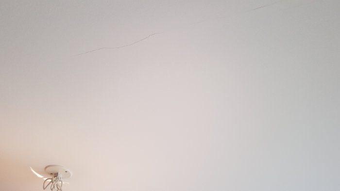 Lång spricka i ett vitt innertak med en taklampa nära sprickans början.