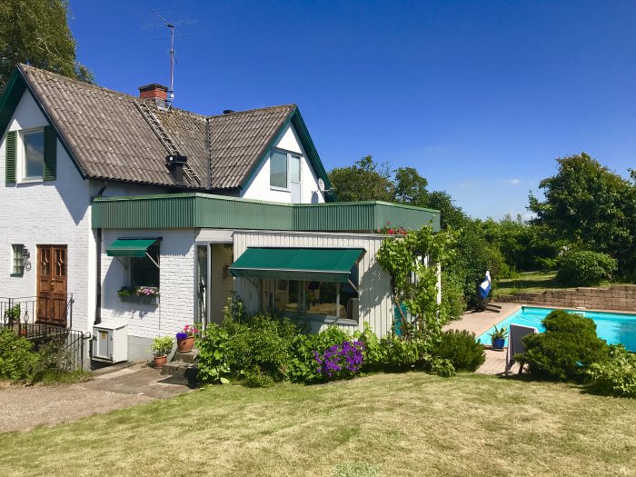 Vitmålat tegelhus från 1926 med grönt tak, pool och trädgård, under renovering.