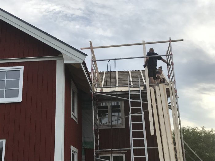 Två personer bygger en träkonstruktion på ett hus under renovering.