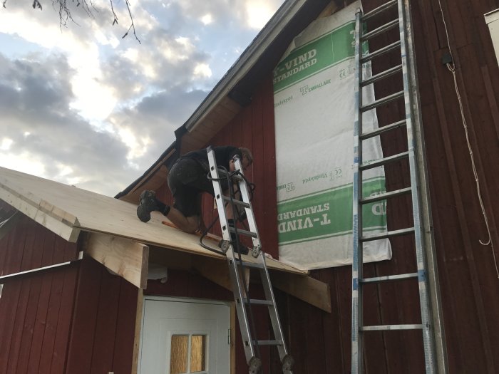 Person som arbetar med takinstallation på en röd stuga, stående på en stege.