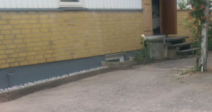 Gult tegelhus med behov av nytt underbleck där gammalt underbleck och ytterpanel möter tegelgrund.