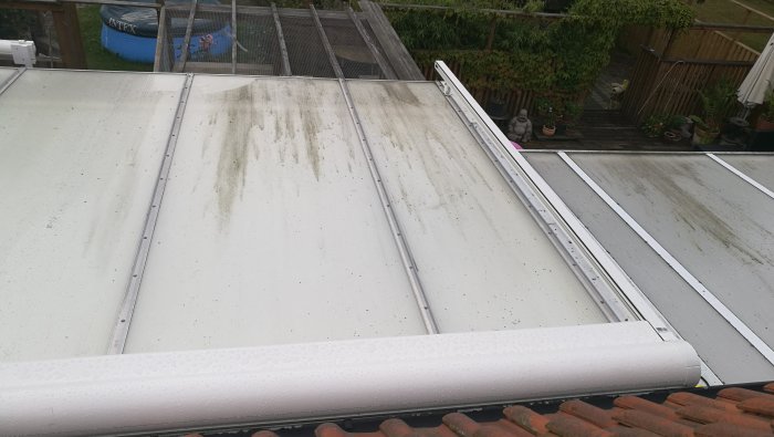 Smutsigt tak av uterum med synliga alger och ojämnheter samt del av terrassmarkis i förgrunden.
