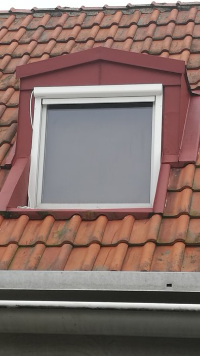 Fönster på övervåning med utdragen terrassmarkis och smutsigt tak av tegelpannor.