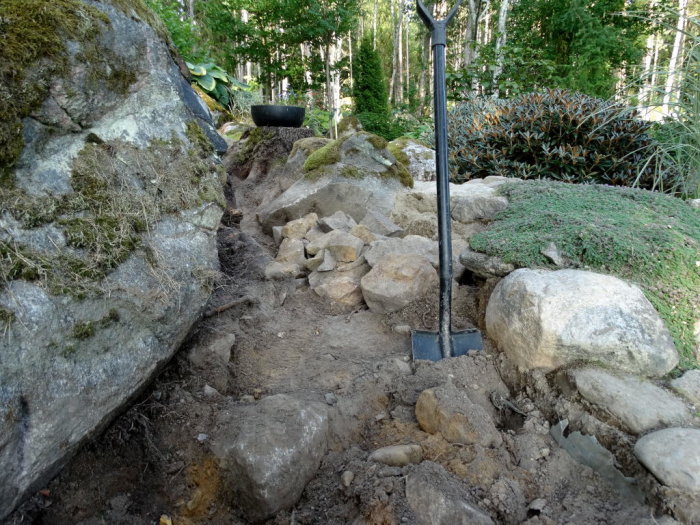 Stenig trädgård med 34 skottkärror jord fylld, redo för plantering, spade i förgrunden.