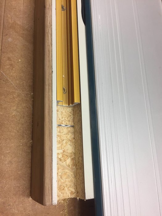 Feljusterad dörr där karmen inte möter golvet korrekt, med synliga spån.