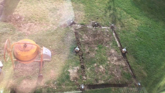 Nybyggd grund för carport med gjutna plintar och betongmixer i trädgården.