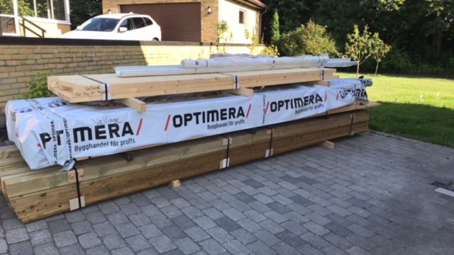 Leverans av byggmaterial från Optimera paketerat och klart för uppförande av en carport, utomhus.