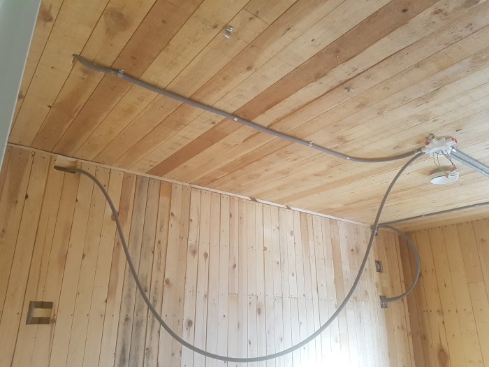 Elektrisk ledning dras längs ett träpaneltak nära en befintlig ledning och armatur i ett renoveringsprojekt.