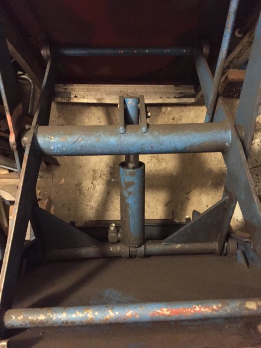Ett blått lyftbord utan hydraulik eller styrning, visande kolven och det slitna metallunderredet.