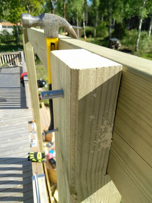 Närbild av träkonstruktion med hammare och vattenpass under pågående pergolabygge.