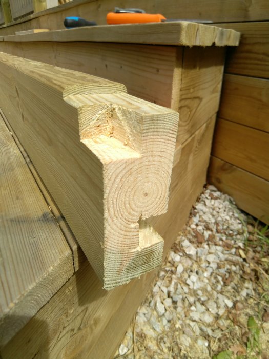 Grovt uthugget hörndetalj på pergola i trä med verktyg i bakgrunden och grus mark.