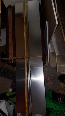 Golvvärmeplåtar i aluminium staplade på golvet med en måttstock bredvid.
