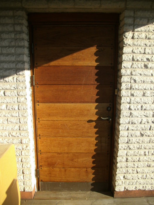 En Bor ytterdörr modell 330 15 i trä monterad i en vit tegelvägg med solljus som skapar skuggmonster.