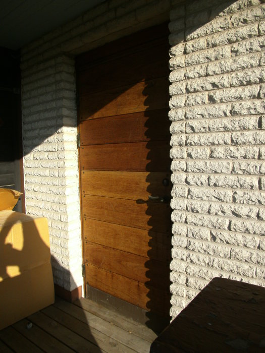 En Bor dörr modell 330 15 av trä mot en vitmålad tegelvägg i solljus med delvis skugga på ytan.