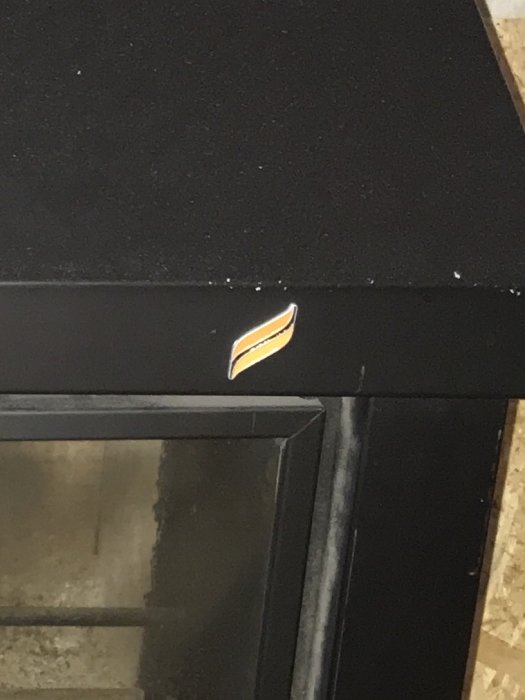 Svart kamin med okänt logotypmärke på kanten, fråga om märke och andrahandsvärde.