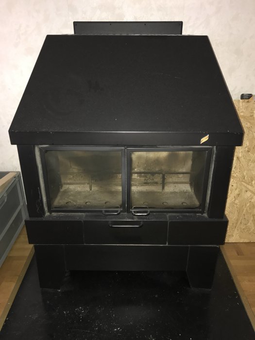 Svart kamin med glasdörrar och asklåda, okänt märke, söker identifiering för andrahandsvärde.