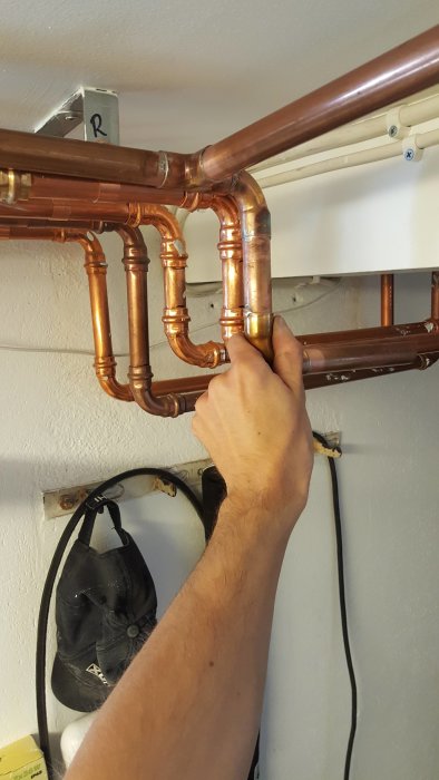 Hand som justerar kopparledningar med T-koppling och böj vid en vägg under renovering.