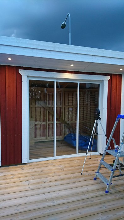 Nyinstallerad skjutdörr i ett hus med röd fasad och vit omfattning, framför en träterrass och en byggstege till vänster.