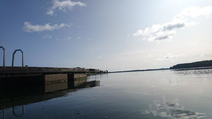 Brygga som sträcker sig över stilla vatten i S:t Anna Skärgård, med moln på himlen.