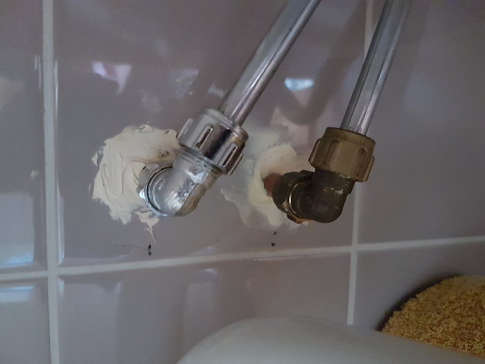 Vattenrör med påfört tätningsmedel och två olika typer av muttrar mot en kakelvägg.