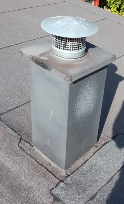 Takgenomföring med grått plåthölje och ventilationstrumma på ett pulpettak med takpapp, exempel på gammalt utförande.