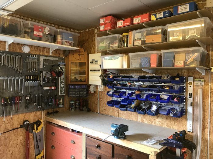Organiserad verkstad med verktygstavla, hyllor med lådor och arbetsbänk.