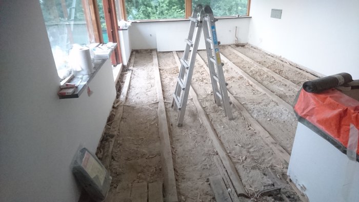 Renoverat rum under ombyggnad med exponerade golvbjälkar och spånskivor, stege i mitten och renoveringsmaterial synligt.