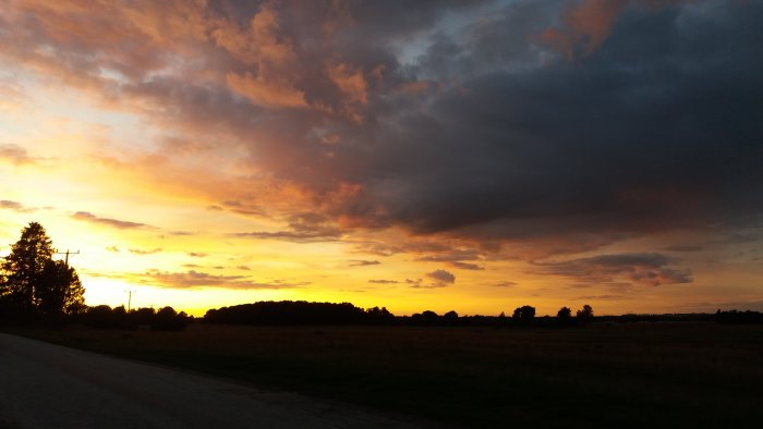 En dramatisk solnedgång med orange-himlen över ett öppet fält och en landsväg.