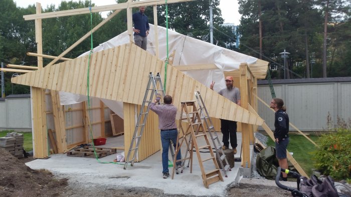 Människor säkrar en trägavelspets på en byggnad med spännband och temporära stödstrukturer.